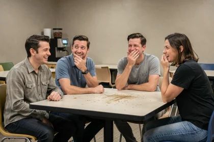Groupe de collègues dans une salle de pause réagissant à une blague gênante avec des rires malaisés et des regards complices