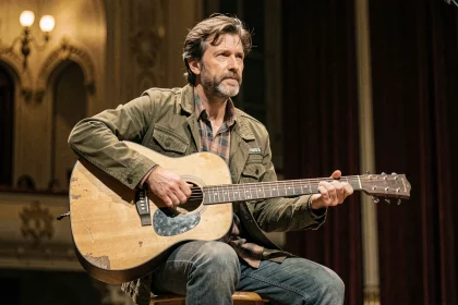 Chanteur français en veste olive jouant de la guitare acoustique sur une scène de concert intime, ambiance nostalgique évoquant la carrière de Renaud
